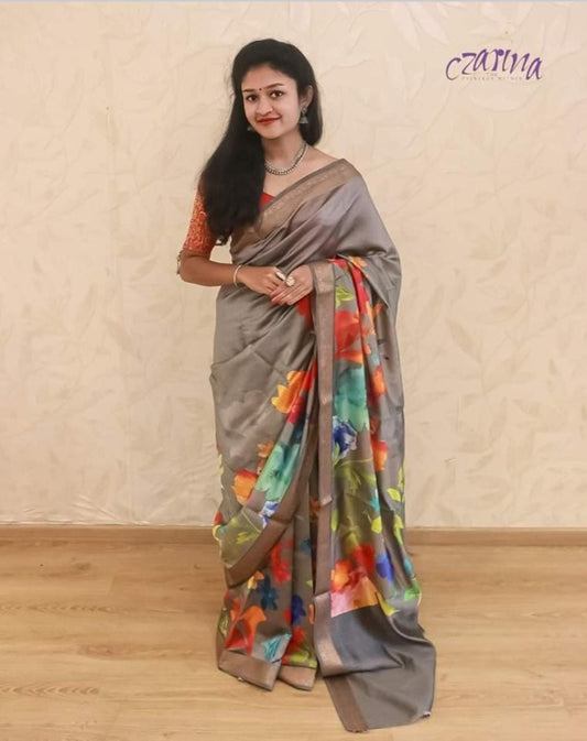 MULTICOLOURED FLORAL PATTERN ADORNS THE SILVER GREY BENARSI  CHINIYA SILK SAREE.